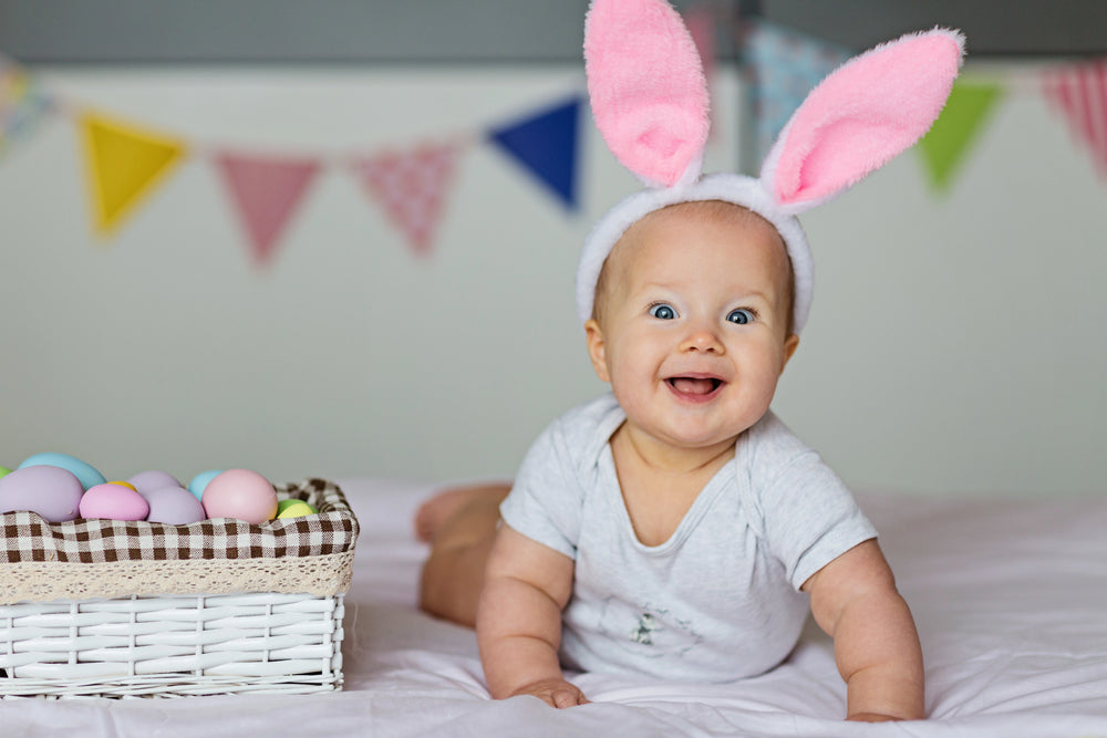 A baby wearing easter bunny ears headband and smiling at the camera. 