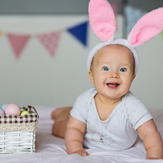 A baby wearing easter bunny ears headband and smiling at the camera. 