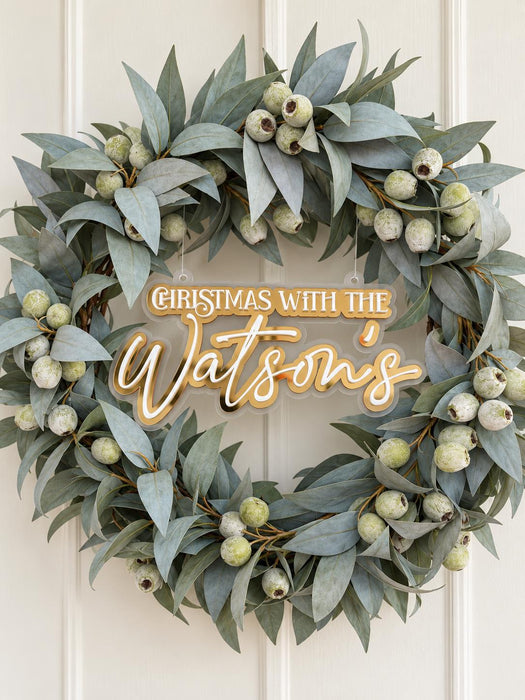 Christmas wreath sign reading Christmas with the Watson's in white and gold mirror acrylic, inside a gum leaf wreath on a door