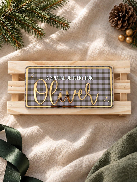 Green gingham name plaque for Oliver with gold mirror lettering, shown straight on against a wooden crate