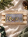 Green gingham name plaque for Oliver with gold mirror lettering, shown straight on against a wooden crate