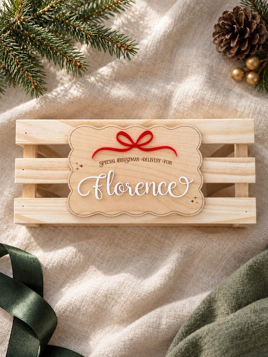 Scalloped wooden name plaque with a red bow reading Special Christmas Delivery For Florence, shown at an angle on a crate