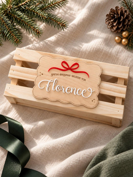 Christmas Eve box plaque in natural wood with a scalloped edge, a red acrylic bow and Florence in white acrylic, on a wooden crate