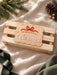 Christmas Eve box plaque in natural wood with a scalloped edge, a red acrylic bow and Florence in white acrylic, on a wooden crate