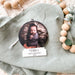 A young baby swaddled in a wrap is sleeping in a photo that has been made into a snow globe shaped Christmas Tree ornament. Their is writing a the base saying Matilda's First Christmas 2021